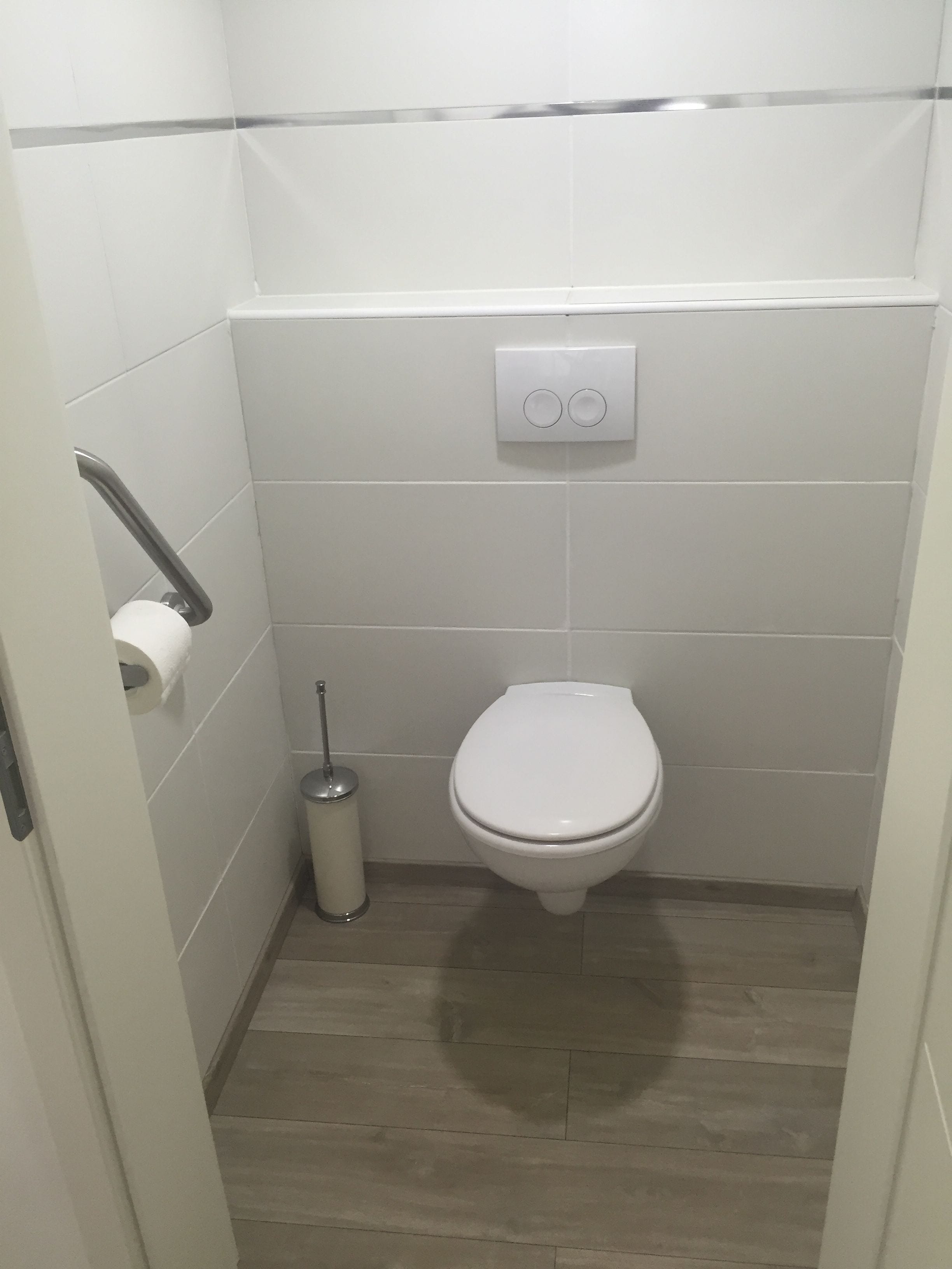 Un baño pequeño y limpio con inodoro, dispensador de papel higiénico y secamanos.