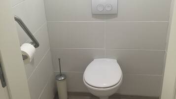 Un baño pequeño y limpio con inodoro, dispensador de papel higiénico y secamanos.