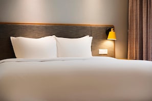 A neatly made bed with white linens and two pillows, a wooden headboard, a wall-mounted lamp, and a power outlet. - Holiday Inn Express DaoCheng Yading (Garze)