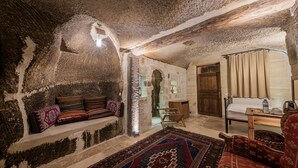Una stanza rustica con una parete in pietra, una panca di legno, un tappeto decorato e una porta in legno.