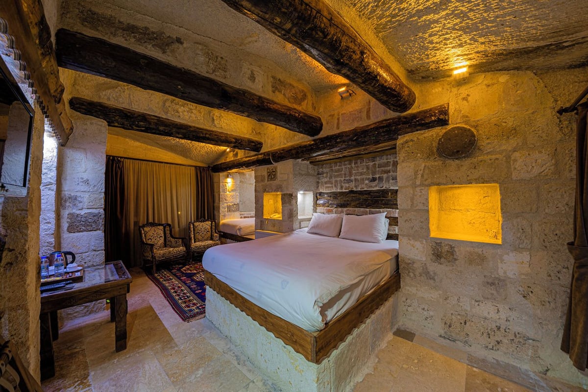 A rustic bedroom with exposed stone walls, a wooden bed frame, and a stone fireplace.
