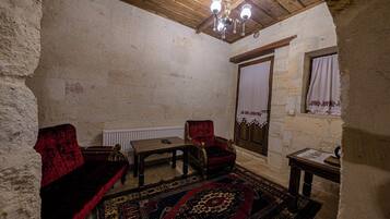 Una habitación rústica con techo de madera, un candelabro, un sofá de terciopelo rojo, una mesa de madera y un tapete estampado.