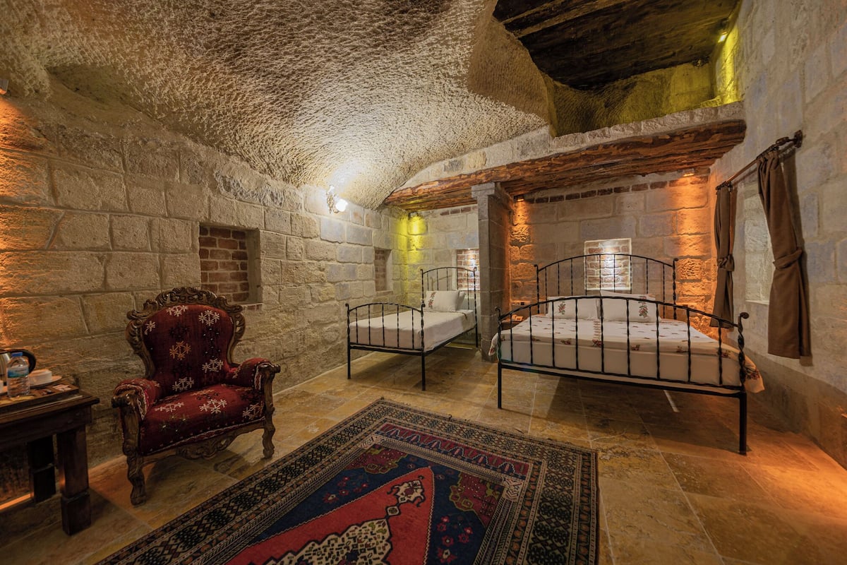 A rustic room with stone walls, a wooden ceiling, and a bed with metal railings.