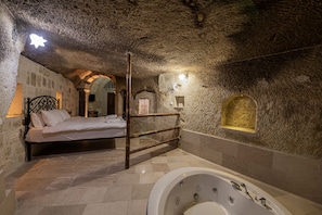 A stone-walled bedroom with a bed, a wooden chair, and a bathtub. - Konak Bezirhane Cave Otel (Ürgüp)