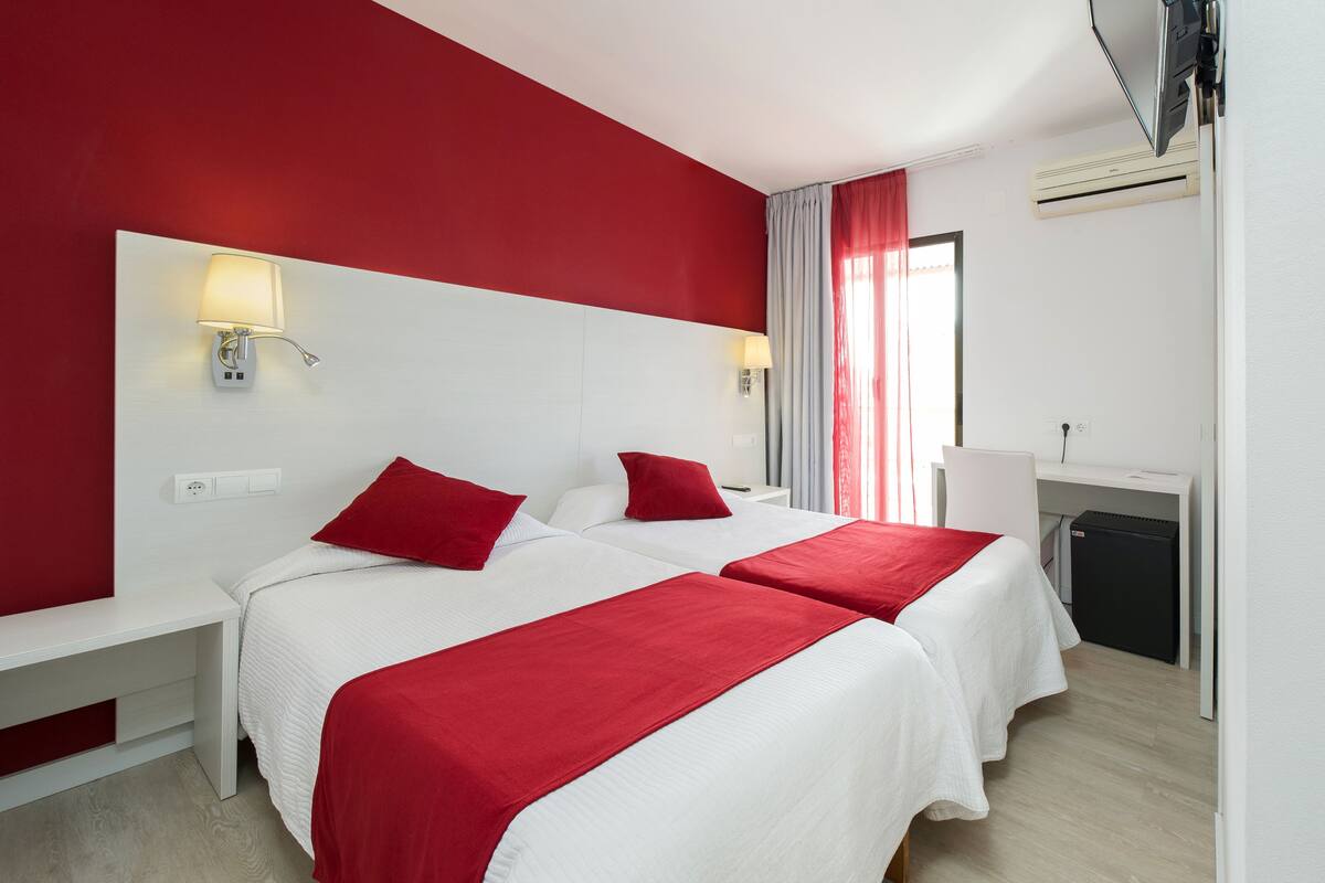 A hotel room with two beds, a desk, and a small refrigerator.