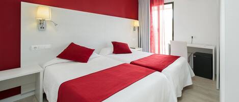 A hotel room with two beds, a desk, and a small refrigerator.