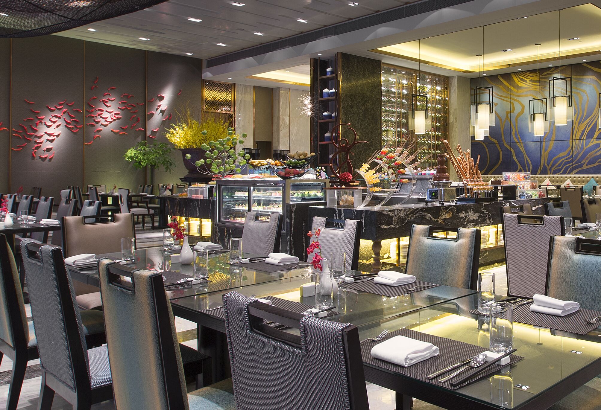 A modern dining area with glass tables, metal chairs, and decorative elements like plants and wall art.