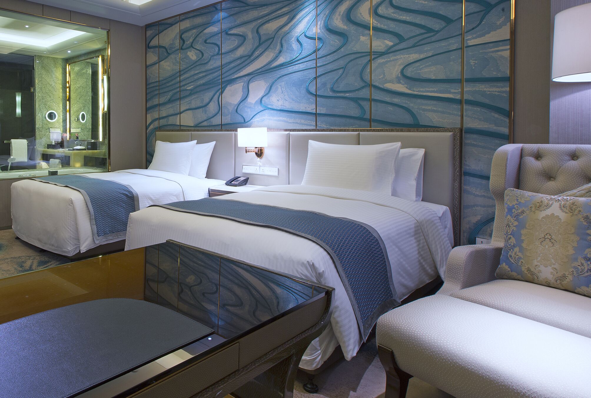 Ein Hotelzimmer mit zwei Betten, einem Schreibtisch, einem Stuhl, einem großen Spiegel und einer Wand mit einem blauen abstrakten Muster.