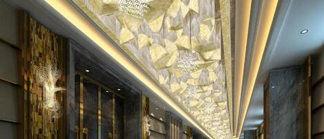 A modern hotel lobby with a long corridor, decorative ceiling, and a patterned carpet.