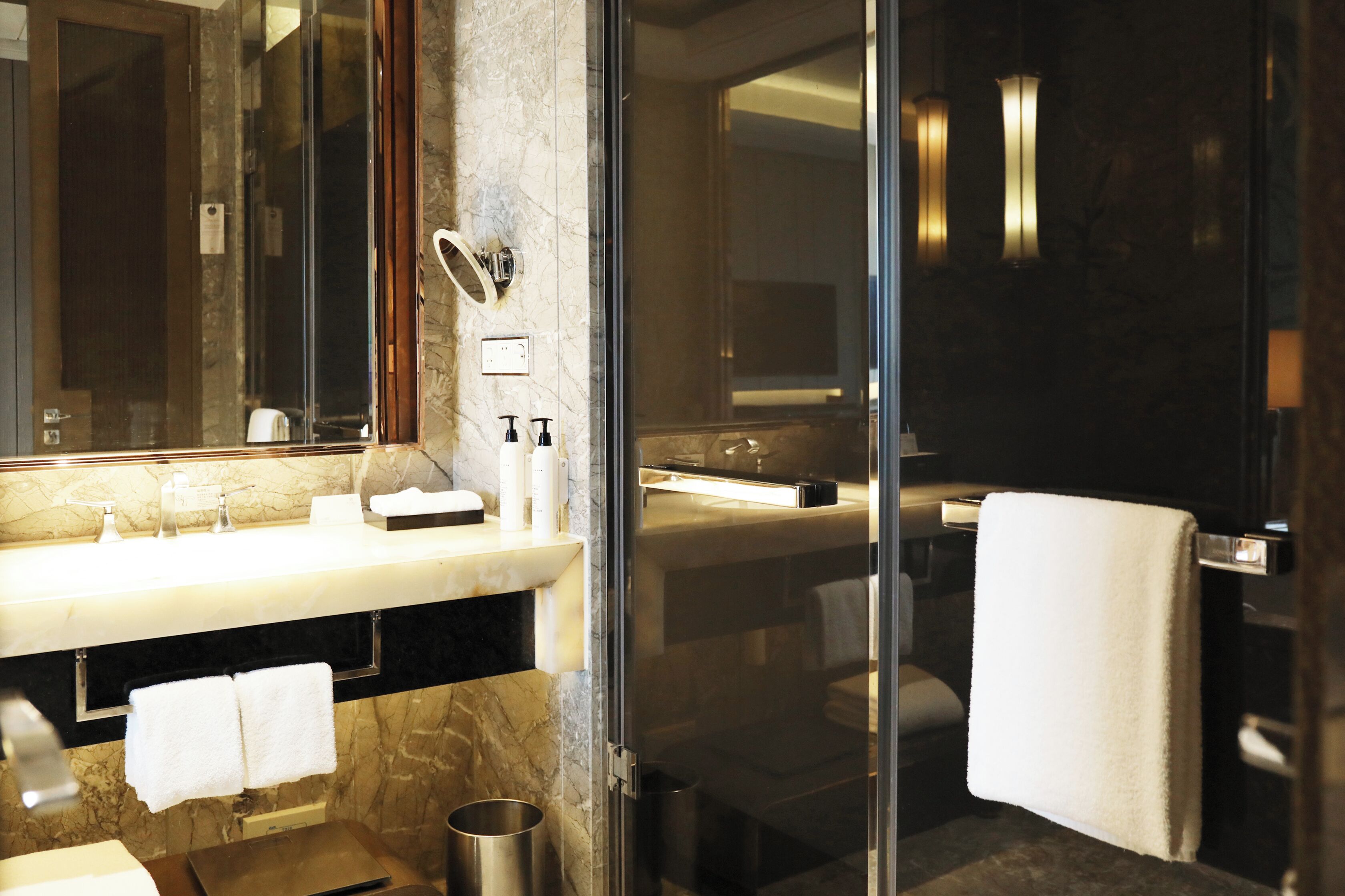 A modern bathroom with a marble vanity, a glass shower enclosure, and a large mirror.