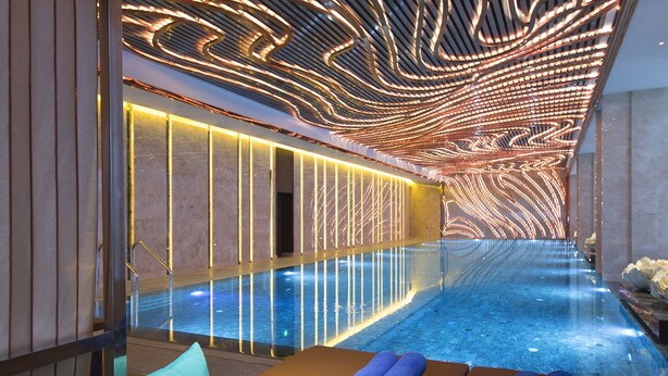 A modern indoor swimming pool with a sleek design, featuring a long, narrow pool area with a glass barrier and a series of illuminated panels on the walls. - Wanda Vista Nanning (Nanning)