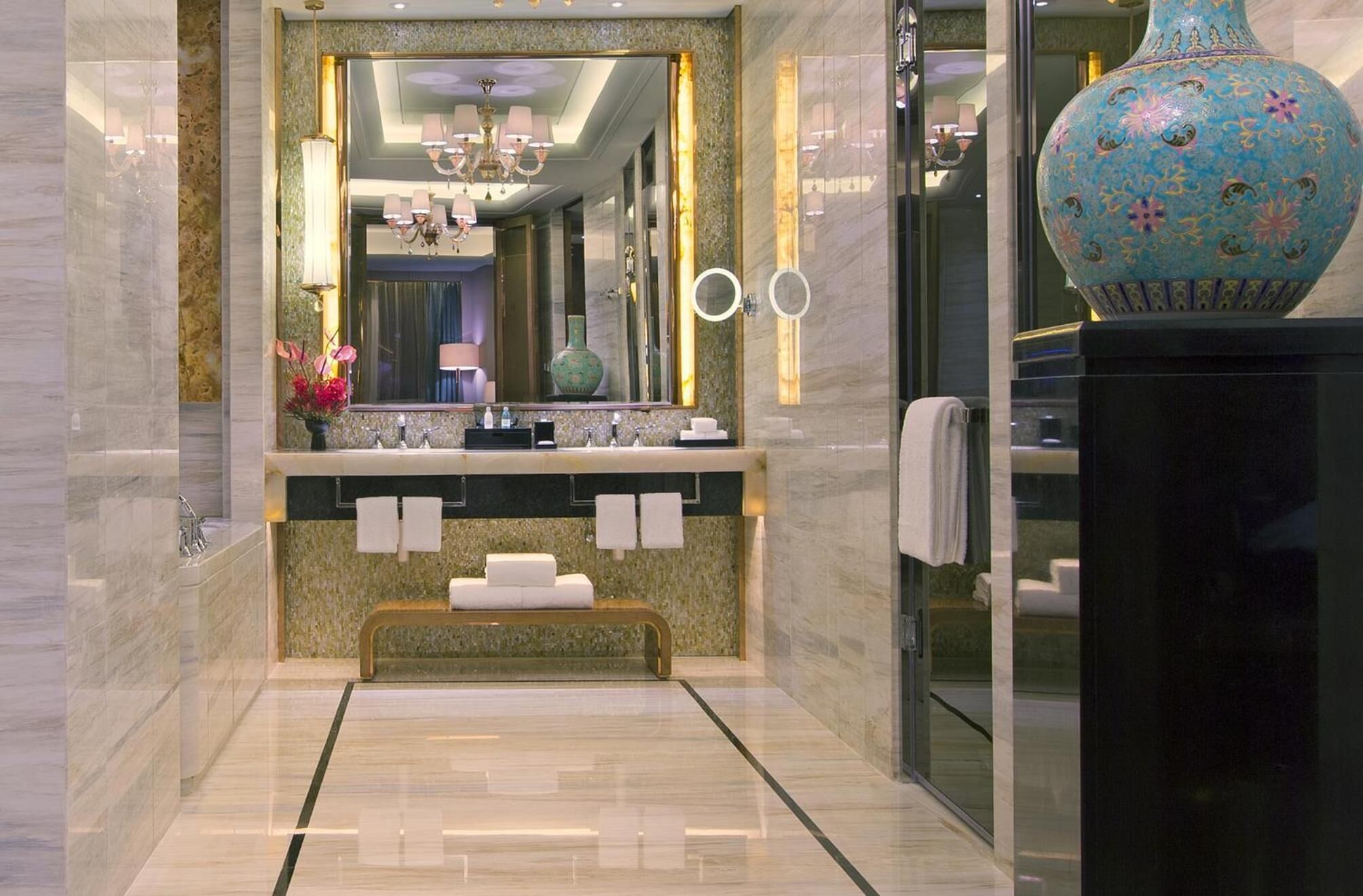 A modern bathroom with a marble floor, a large mirror, a vanity with a sink, and a decorative vase.