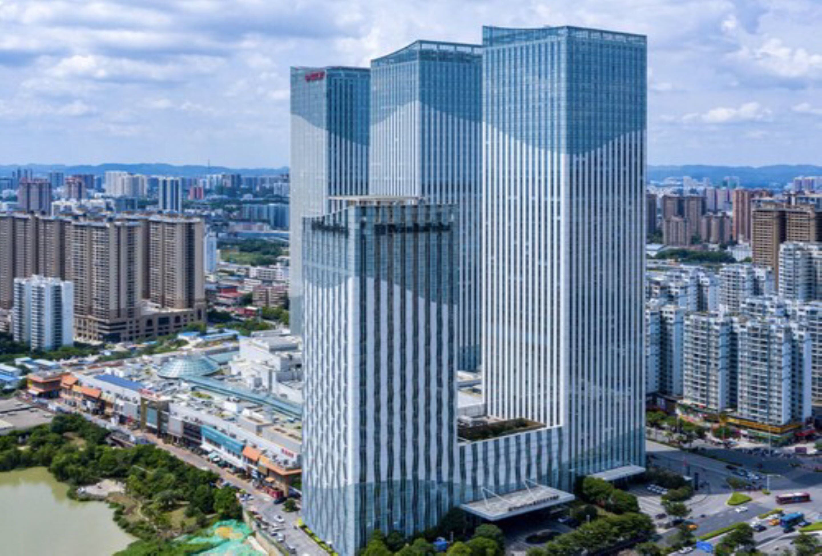 Un edificio de gran altura con fachada de vidrio moderna, rodeado de otros edificios altos y una masa de agua.