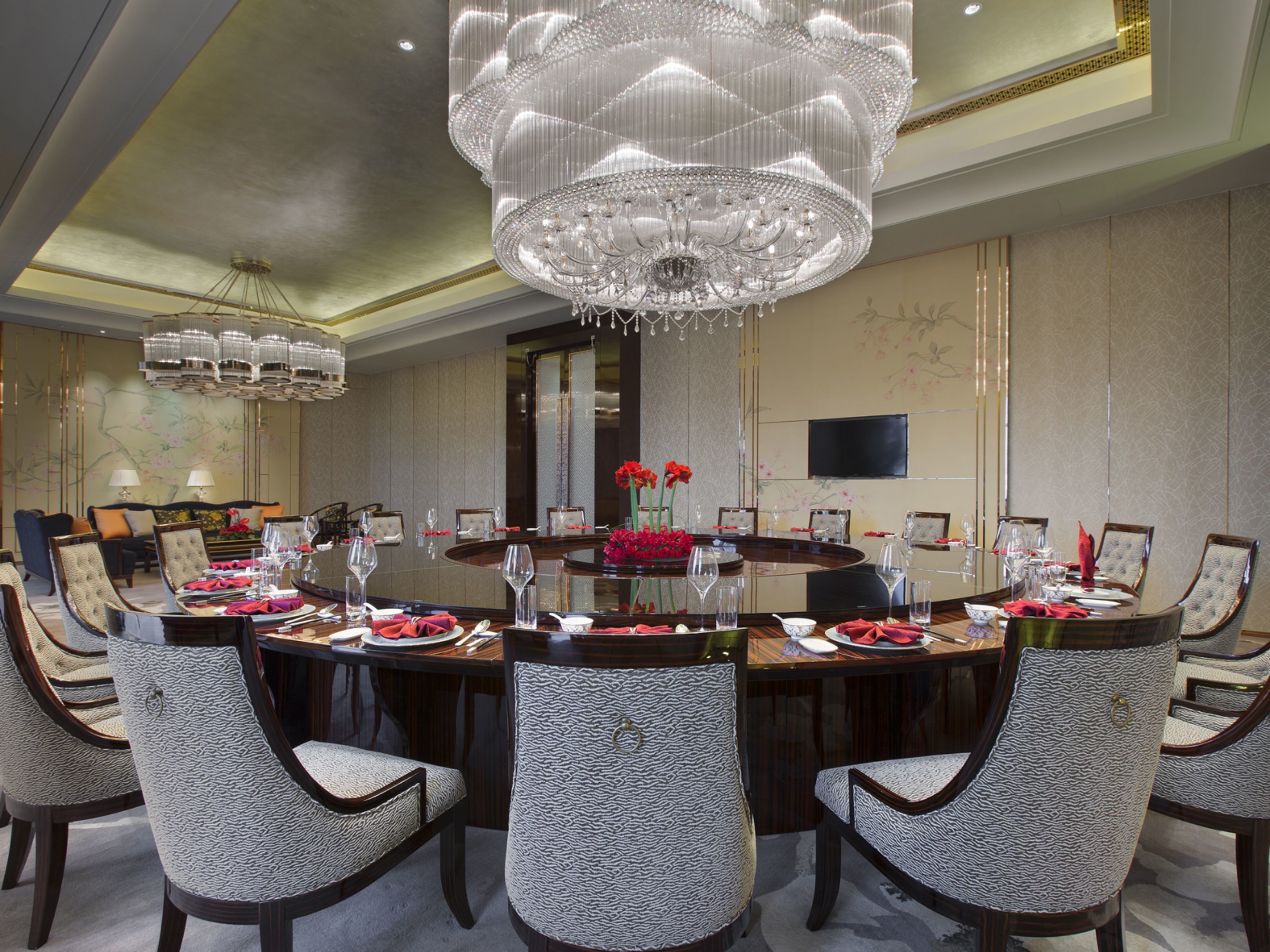A formal dining room with a large round table, multiple chairs, and a grand chandelier.