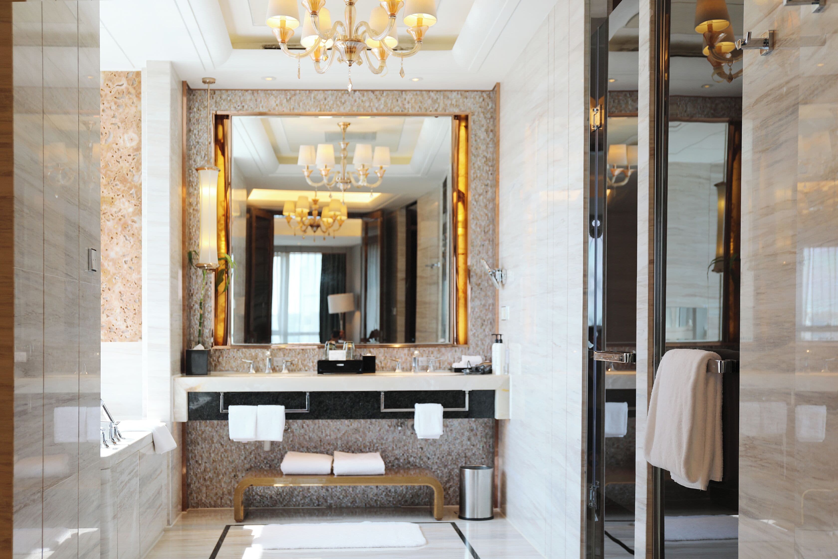 A modern bathroom with a large mirror, a bench, and a glass shower enclosure.