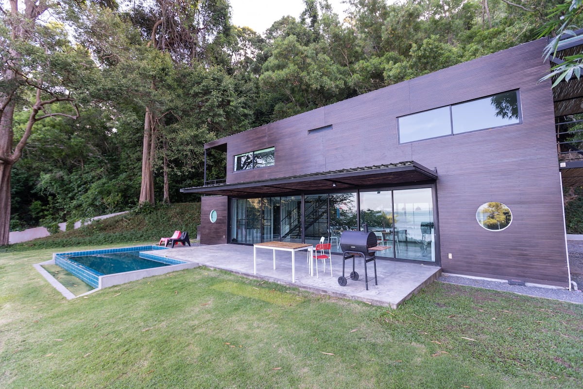 Una casa moderna con piscina, mobiliario exterior y zona de barbacoa.