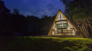 Un edificio de forma triangular con grandes ventanales y un interior bien iluminado, rodeado de vegetación.