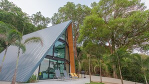 Una casa moderna con techo inclinado, amplios ventanales y una zona de piscina con sillones de descanso.