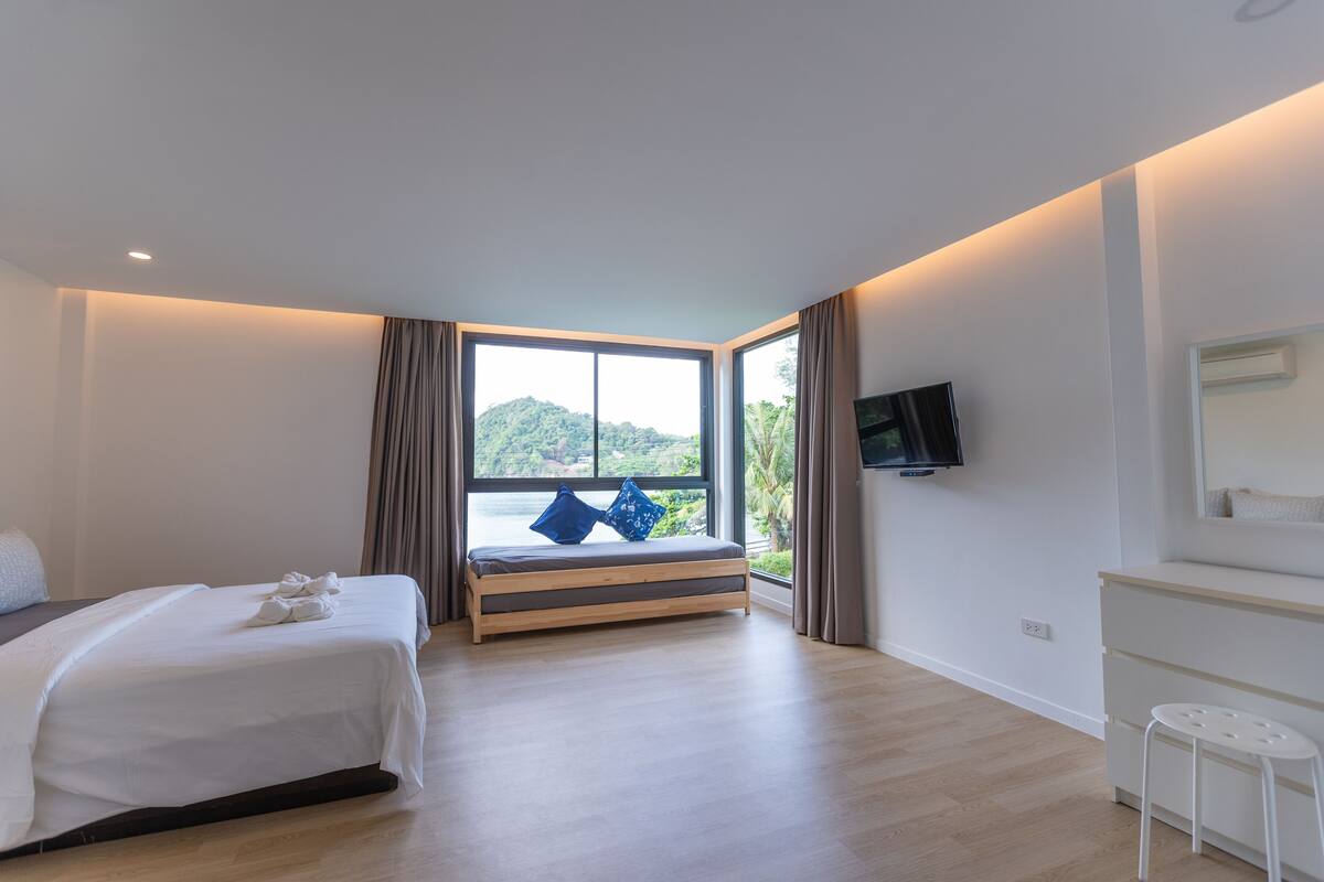 Habitación de hotel moderna con cama, televisión, escritorio y un amplio ventanal con vistas a zonas verdes.
