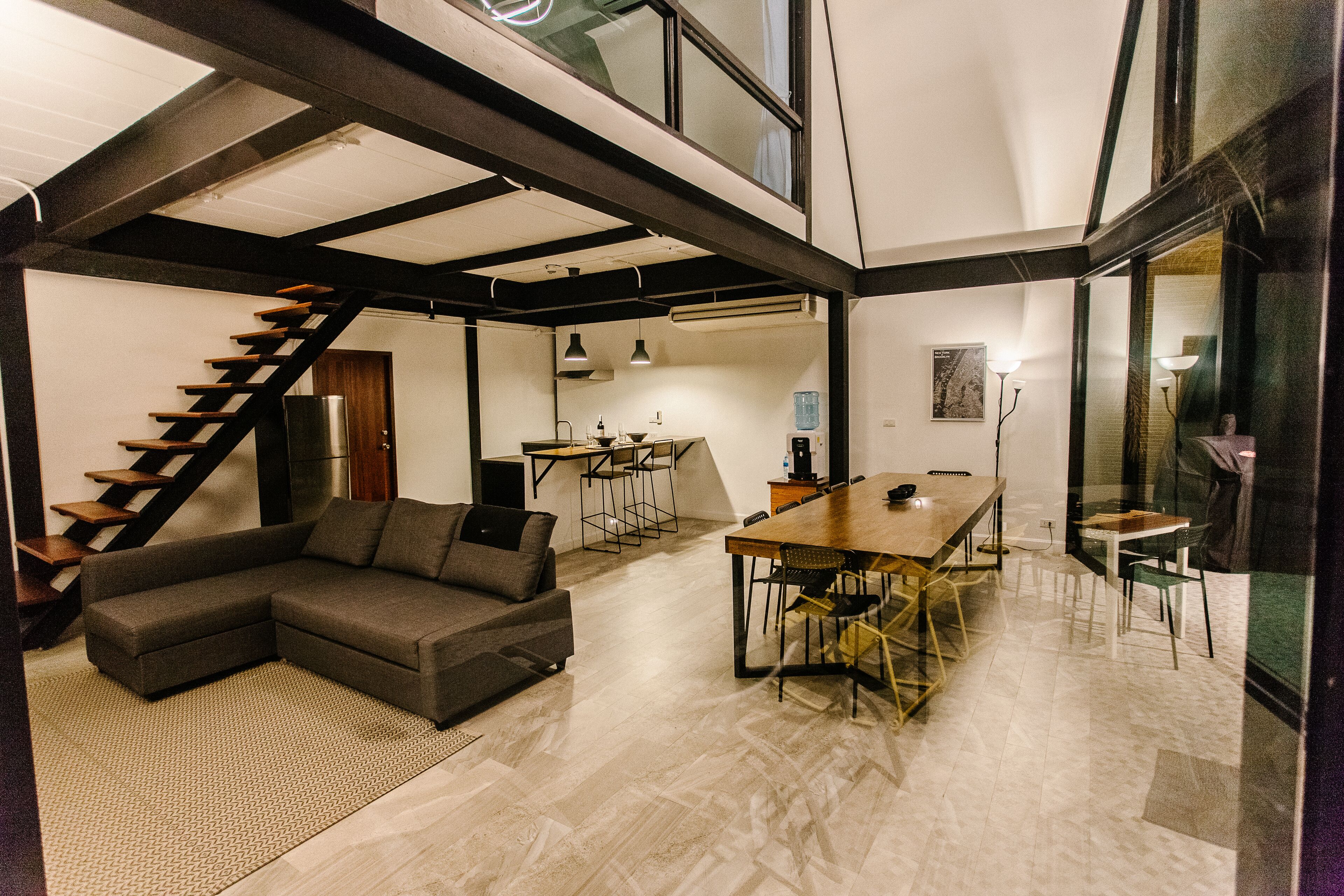A modern living space with a staircase, a sectional sofa, a dining table, and a kitchen area.