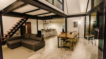 A modern living space with a staircase, a sectional sofa, a dining table, and a kitchen area.