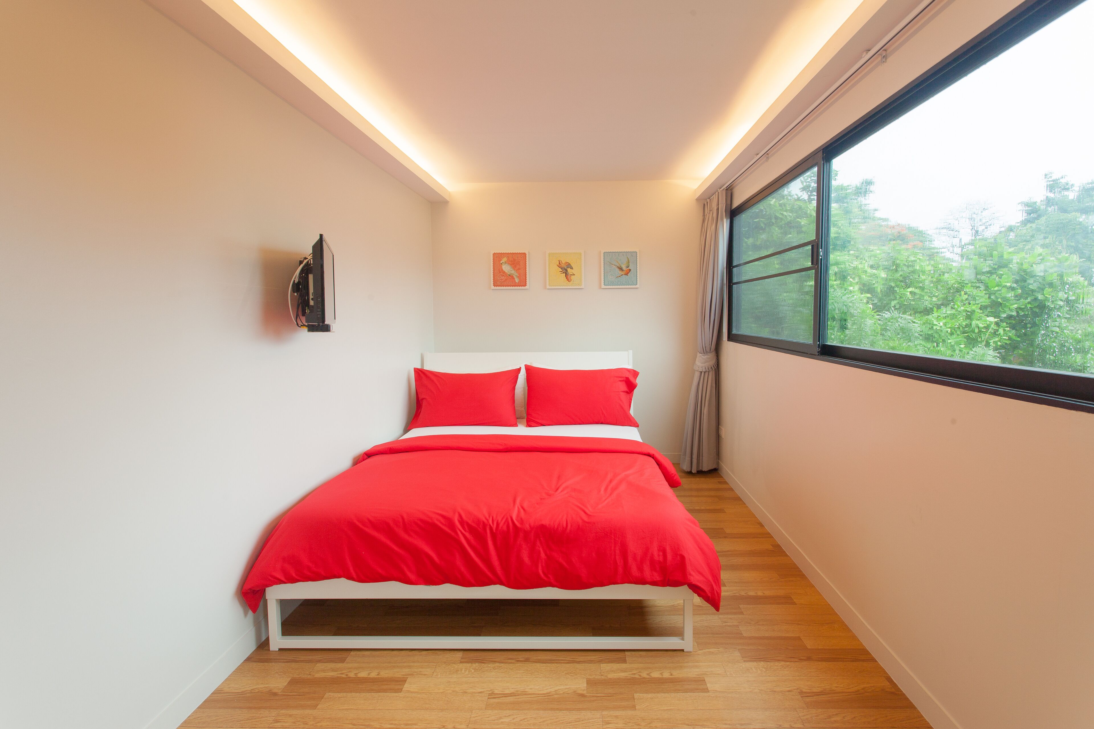 Ein Schlafzimmer mit Bett, Fernseher und einem Fenster mit Blick auf Bäume.