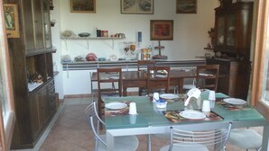 Un comedor con mesa de vidrio, sillas de metal y sillas de madera. Se observan cuadros en la pared y un aparador con puertas de cristal.