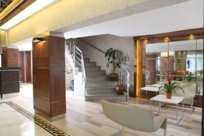 A modern lobby with a staircase, a reception desk, and a seating area with a plant. - Sultan Hotel - Restaurant (Sivas)