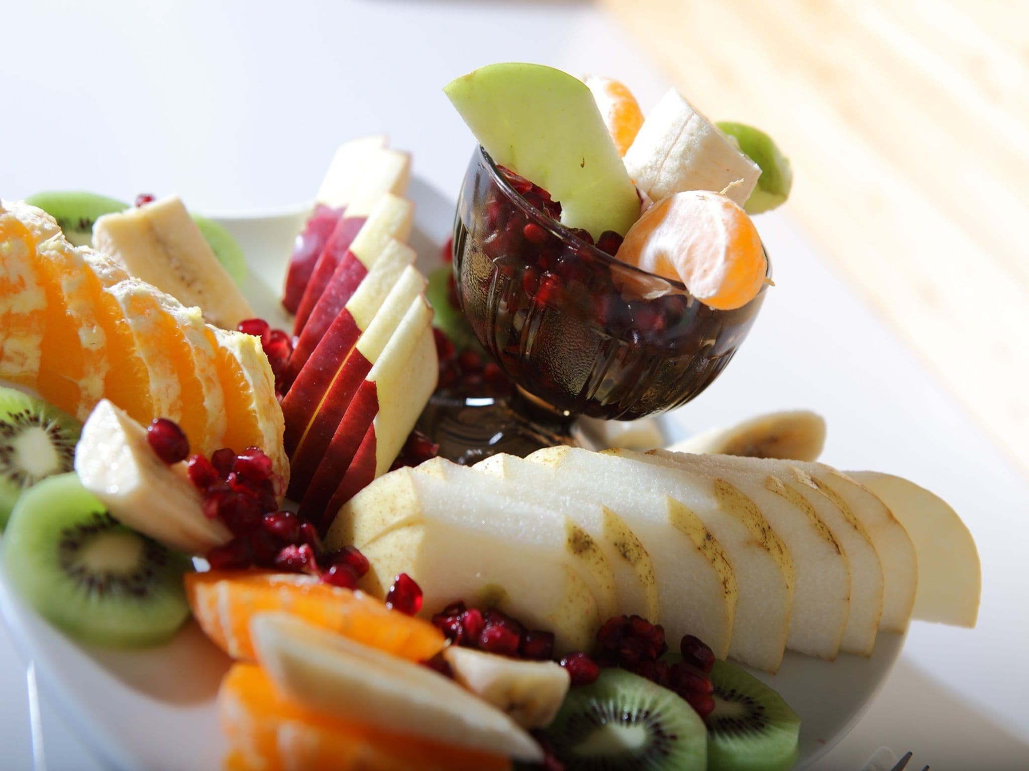 A fruit platter with sliced apples, oranges, kiwi, and pomegranate seeds, accompanied by a glass of juice.