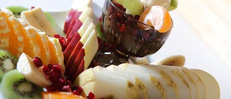 A fruit platter with sliced apples, oranges, kiwi, and pomegranate seeds, accompanied by a glass of juice.