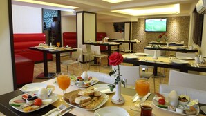 Ein Hotelrestaurant mit roten Sitzgelegenheiten, einem Frühstücksbuffet und einem Fernsehbildschirm.