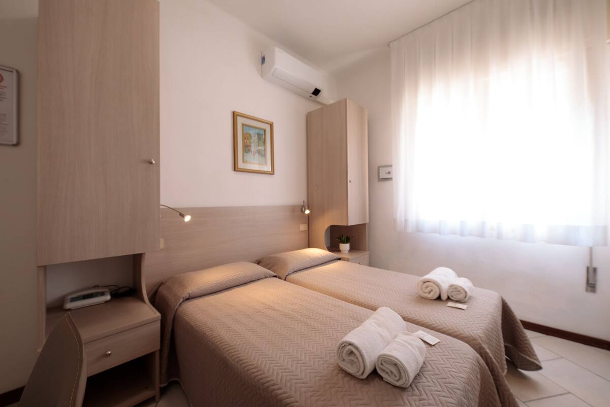 Une chambre d’hôtel avec deux lits, une table de chevet, une armoire et une fenêtre avec des rideaux.