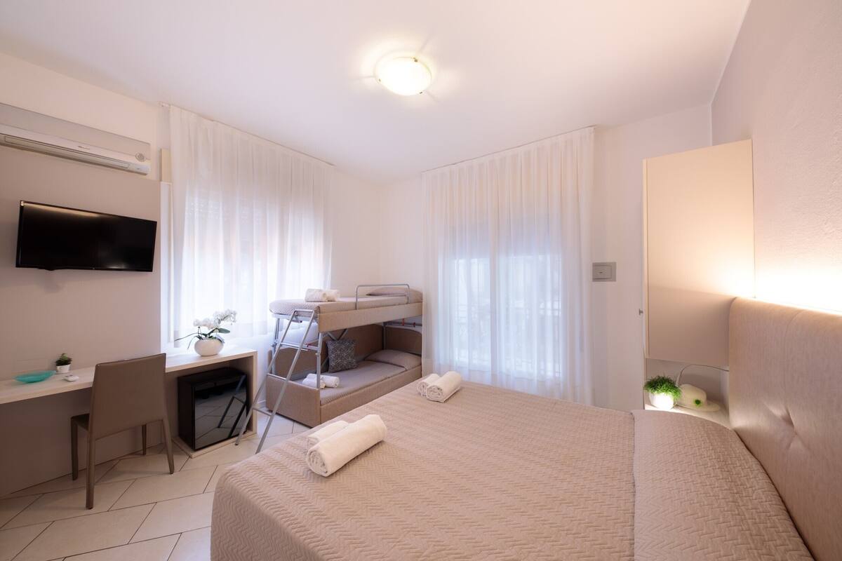 Une chambre d’hôtel comprenant un lit, un bureau avec une chaise, un téléviseur fixé au mur et un lit superposé.