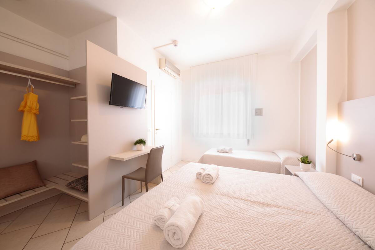 Une chambre d’hôtel moderne équipée d’un lit, d’un bureau, d’une télévision et d’une fenêtre avec des rideaux légers.