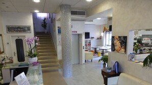 A reception area with a staircase, a reception desk, a white sofa, and a painting on the wall. - Hotel Madison (Jesolo)