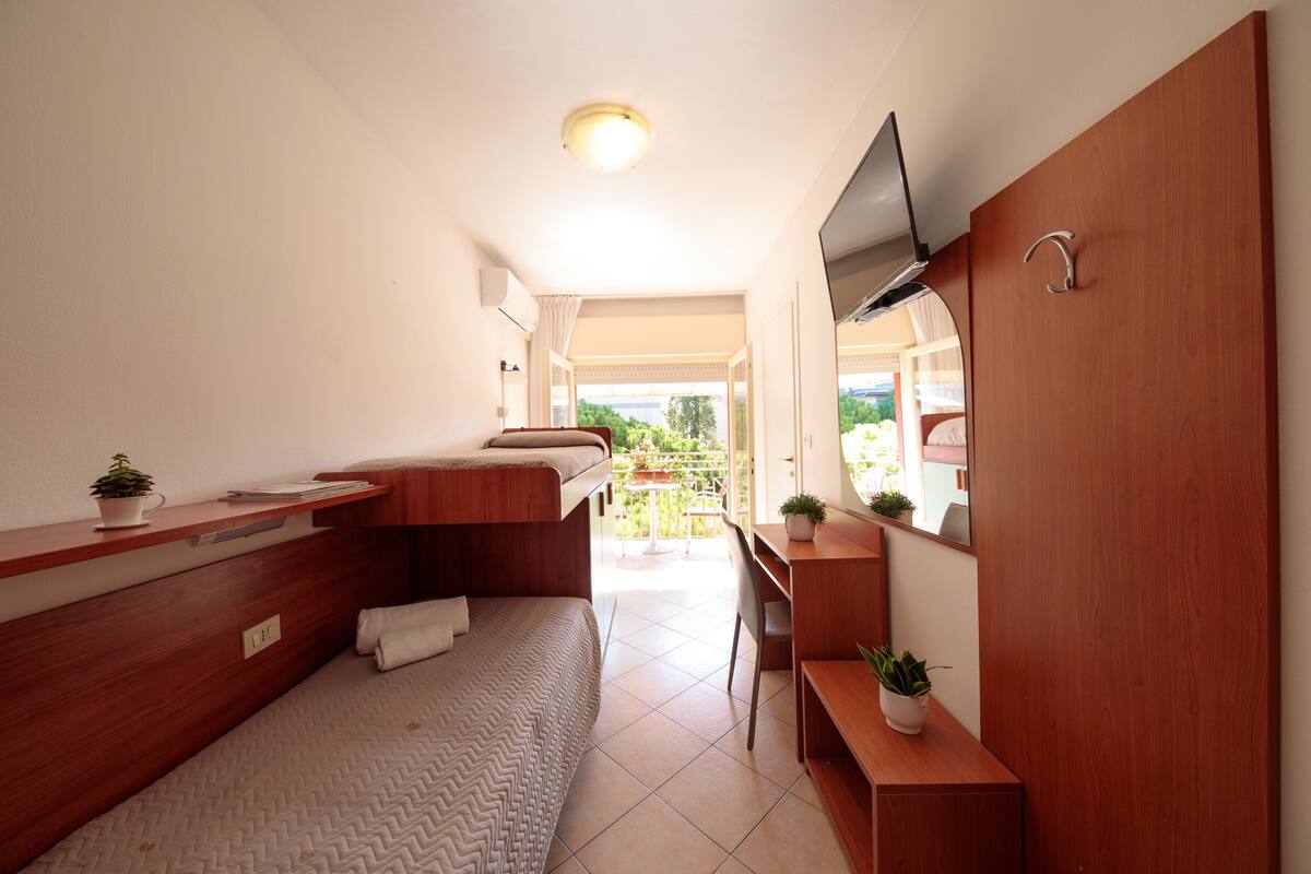 Une chambre d’hôtel compacte comprenant un lit, un bureau, une télévision et un balcon avec vue.