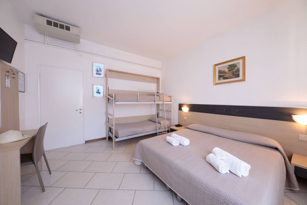 Une chambre d’hôtel avec des lits superposés, un bureau et un lit avec des serviettes roulées.
