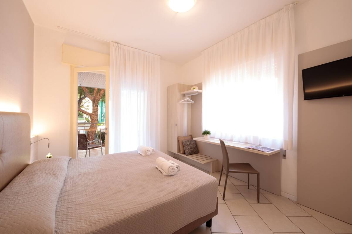 Une chambre d’hôtel avec un lit, un bureau et une chaise, une télévision et une fenêtre avec des rideaux.