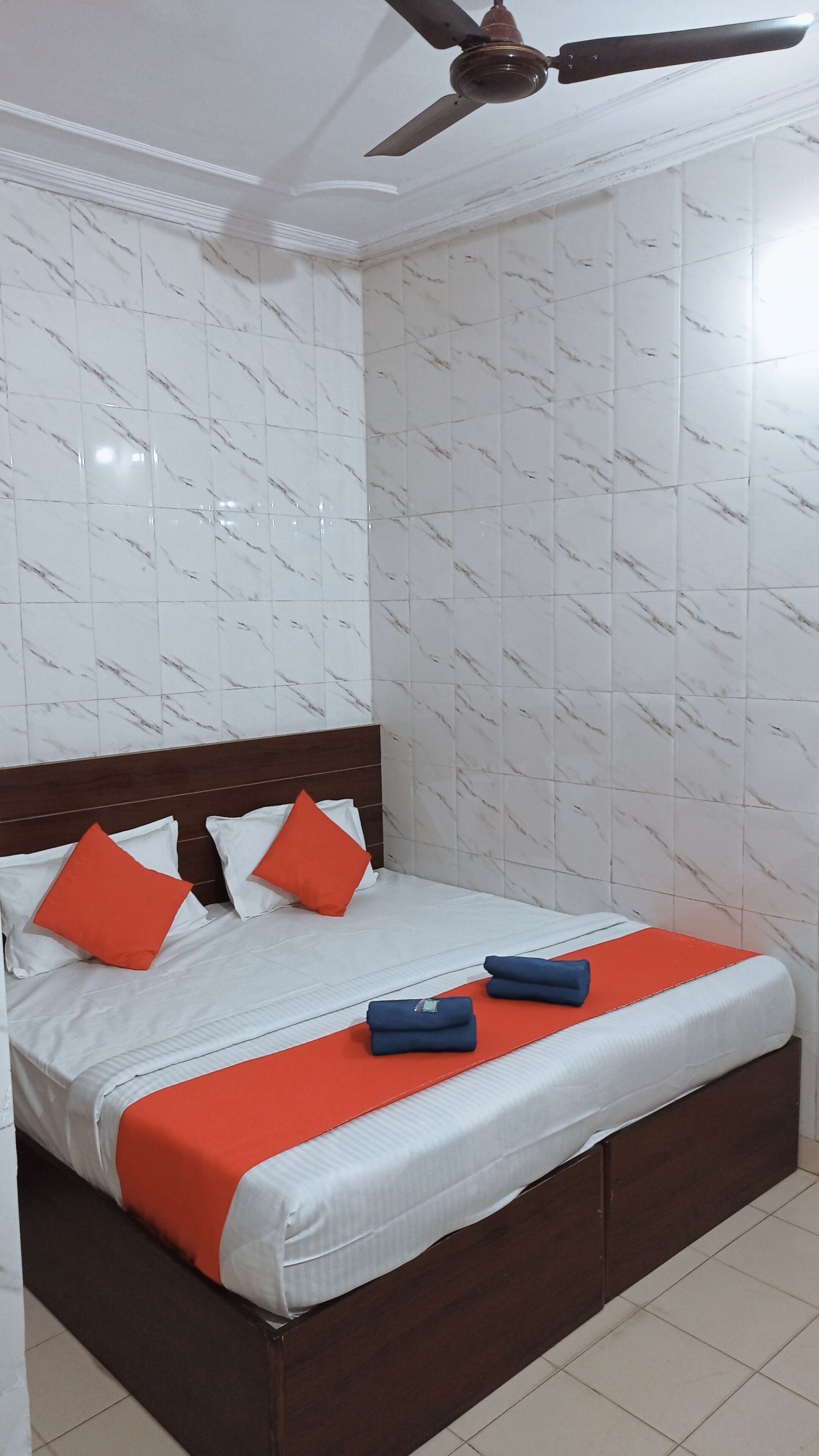 Una cama bien hecha con cabecera de madera, ropa de cama blanca y almohadas naranjas y rojas.