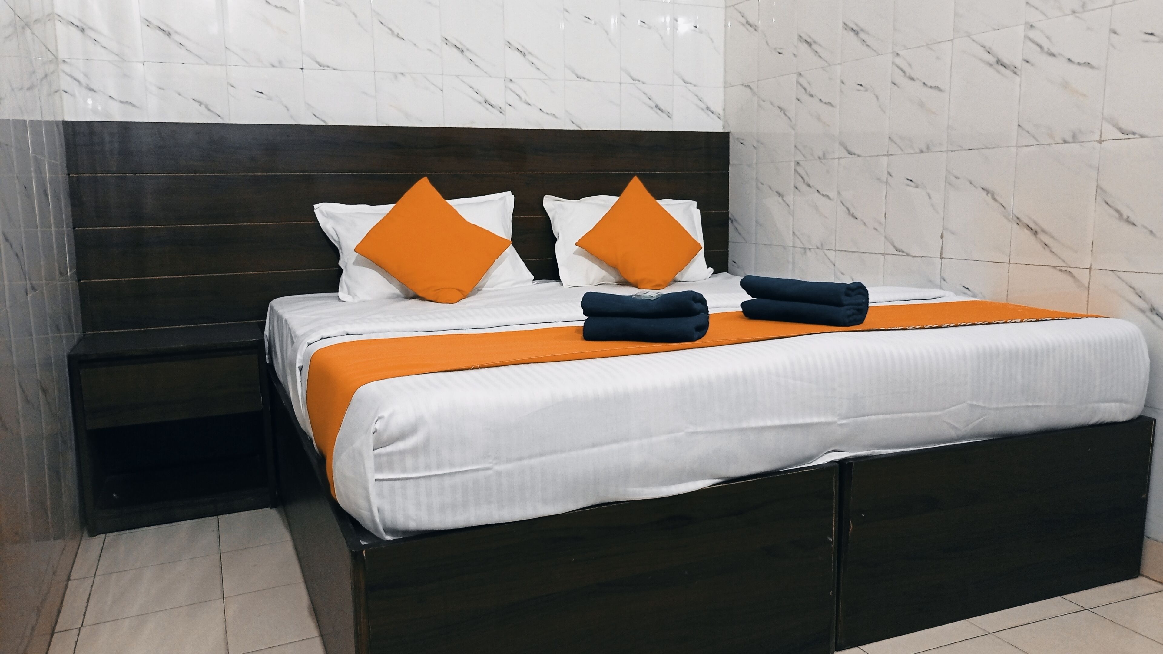 A hotel room with a dark wood headboard, white bedding, and orange accents.