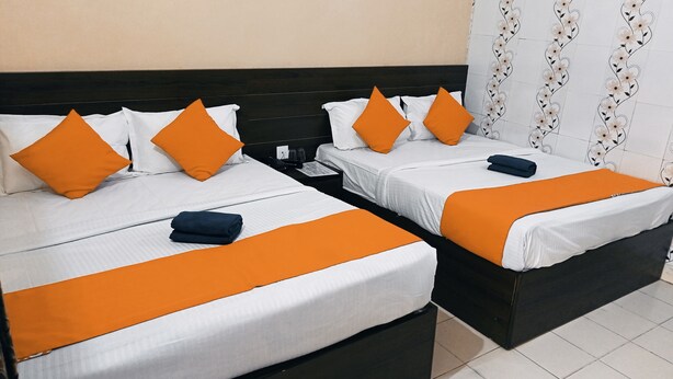 A hotel room with two beds, each with white bedding and orange accents, a dark headboard, and a nightstand with a phone and glasses. - Hotel Bharat Palace (Jaipur)