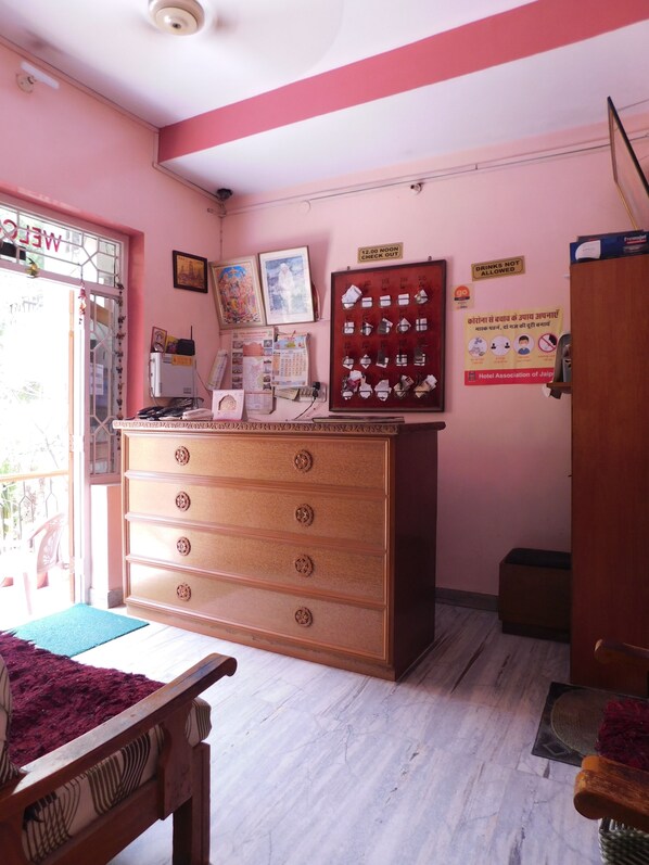 A hotel room with a wooden dresser, a desk with a computer, a window with a view, and a door. - Hotel Bharat Palace (Jaipur)