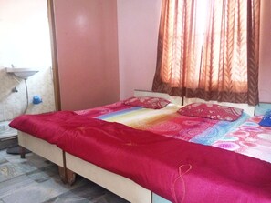 A bedroom with a bed, pillows, a window with curtains, a bedside table, and a wall-mounted sink. - Hotel Bharat Palace (Jaipur)