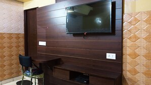 A room with a TV mounted on a wooden wall, a small table, and a chair. - Hotel Bharat Palace (Jaipur)