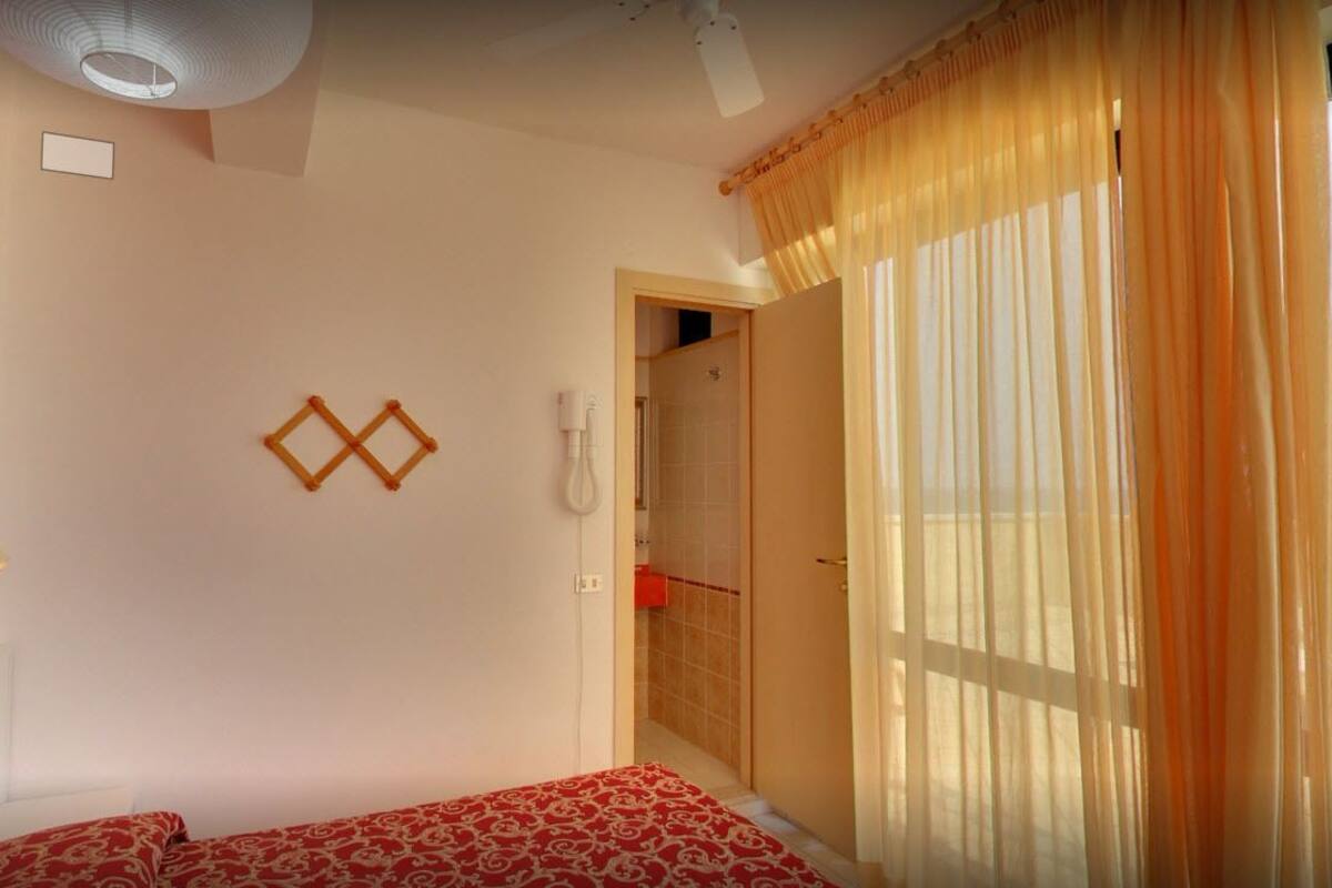 Ein Schlafzimmer mit einem Bett, einem an der Wand befestigten Telefon und einer Tür zu einem Badezimmer.