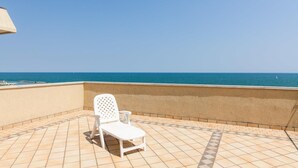 Ein weißer Lounge-Sessel auf einem gefliesten Balkon mit Blick aufs Meer.