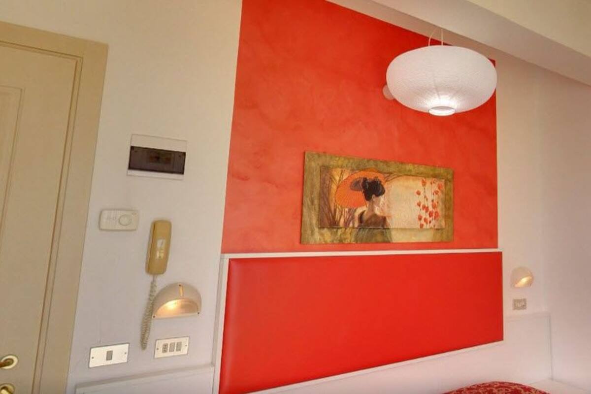 Ein Zimmer mit einer roten Akzentwand, einem Gemälde, einer weißen Deckenleuchte, einem Telefon und einer Wandleuchte.
