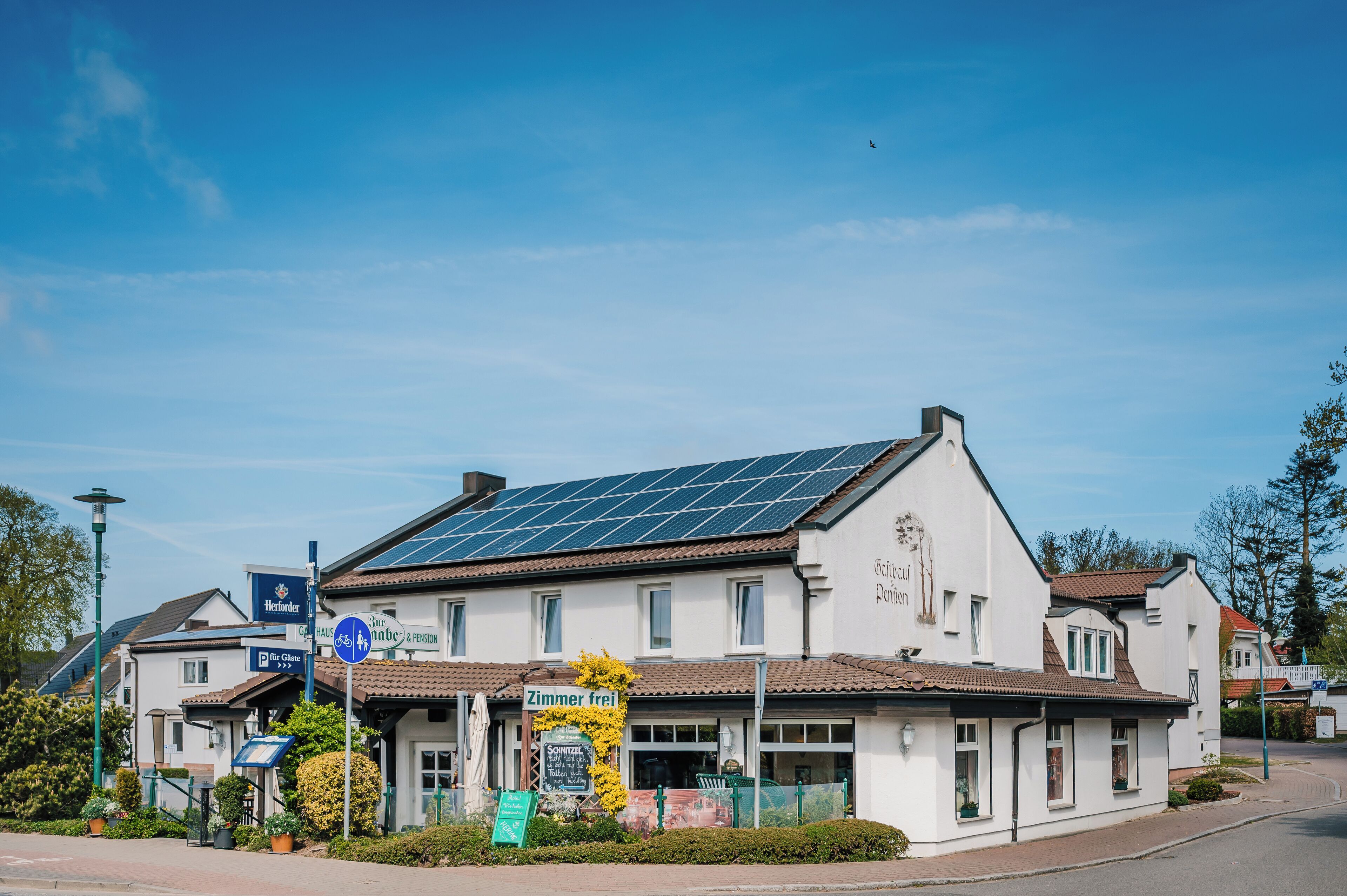 A white building with solar panels on the roof, a sign for 'Zimmer frei', and a 'Herforder' sign.