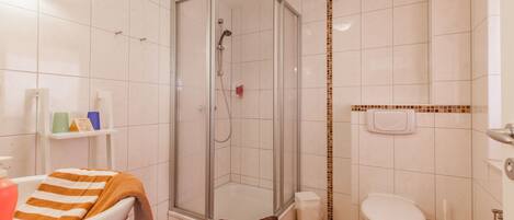 A bathroom with a glass-enclosed shower, a white toilet, and a sink with a towel.