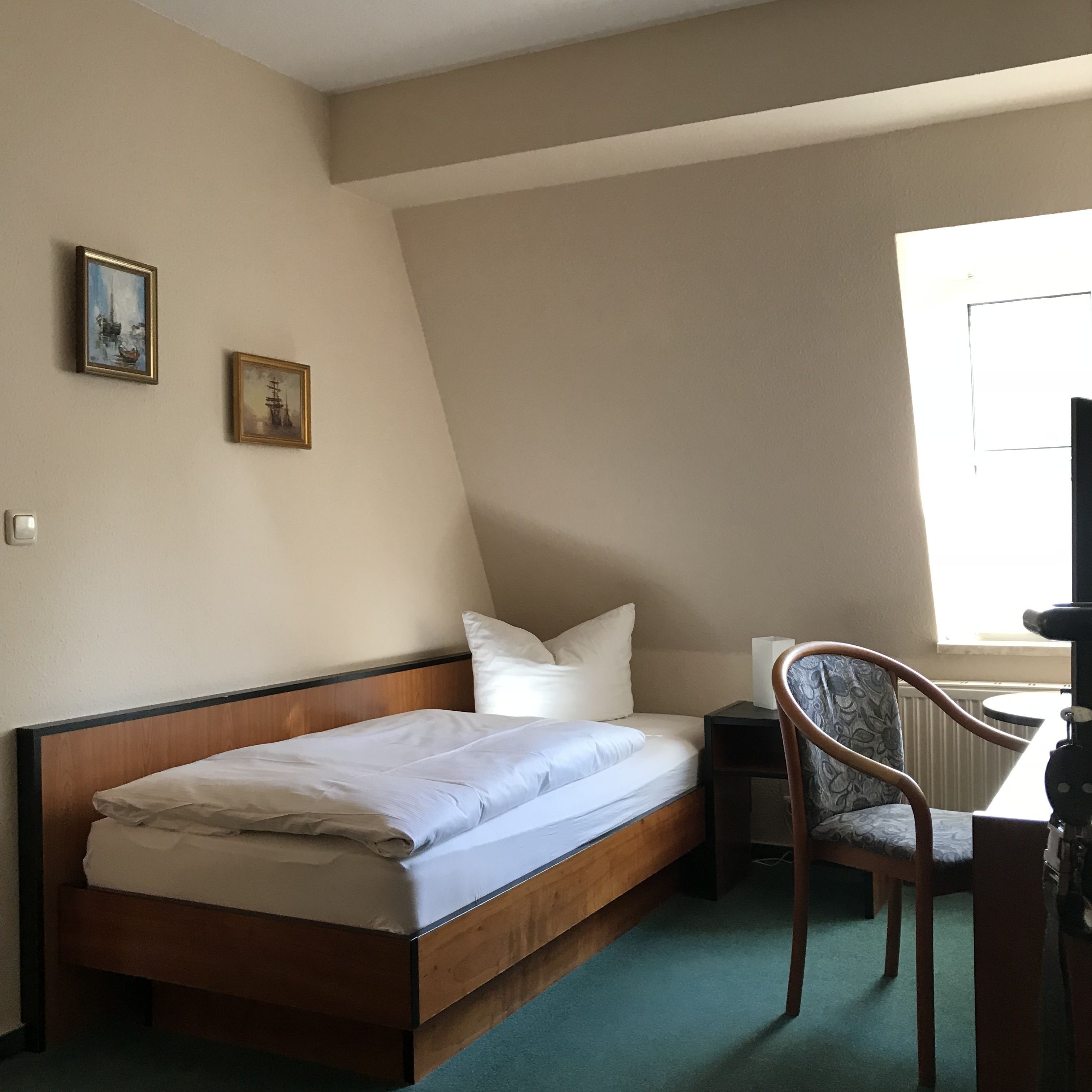 A small, neatly made bed with white linens, a wooden headboard, and two framed pictures on the wall.
